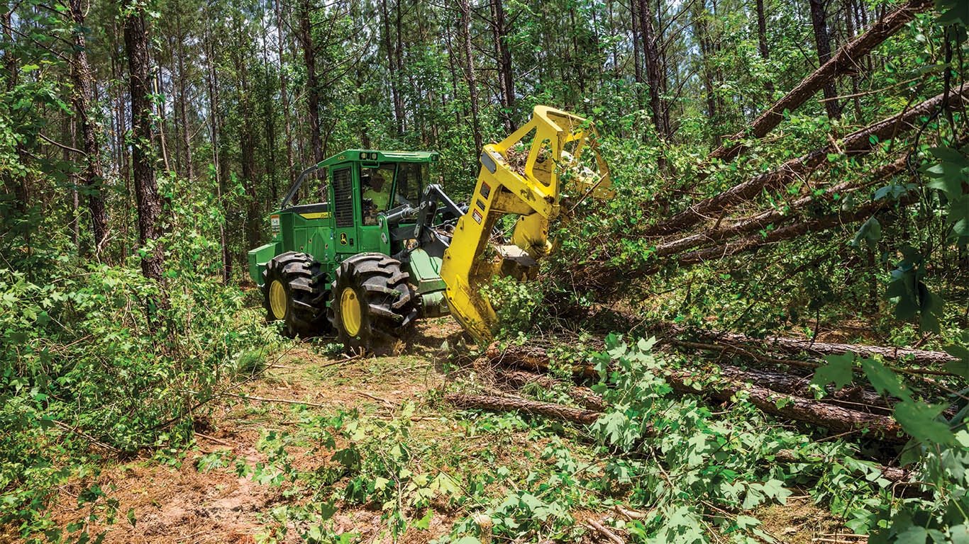 A John&nbsp;Deere tracked felled buncher felling a tree in a forest.
