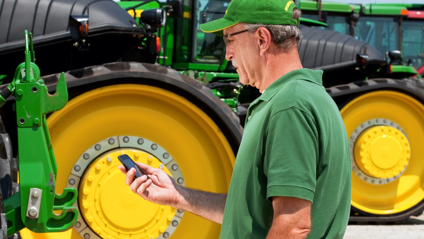 man holding smart phone next to a tractor